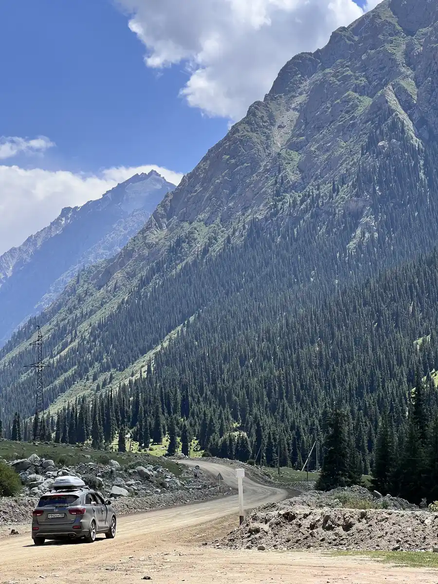 SUV driving a dirt road through Barskoon Gorge with forested mountains around